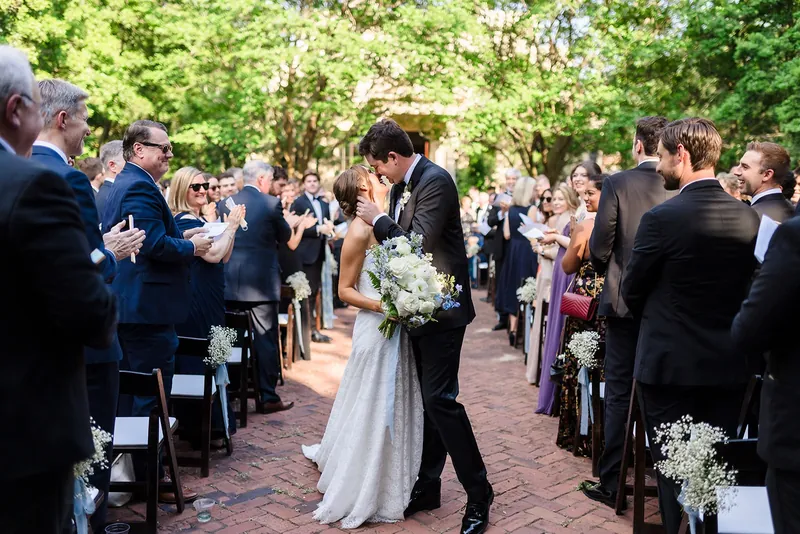 Couple walking back down a garden aisle as guests cheer